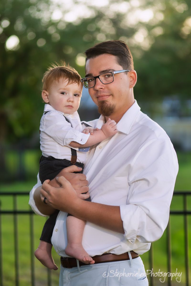 Man in white shirt holding a dressed-up baby boy outdoors, professional family portrait by Stephannie Photography.