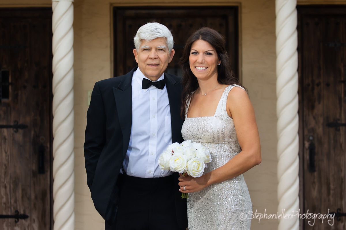 Elegant bride in a silver gown holding white peonies posing with an older gentleman in a tuxedo.