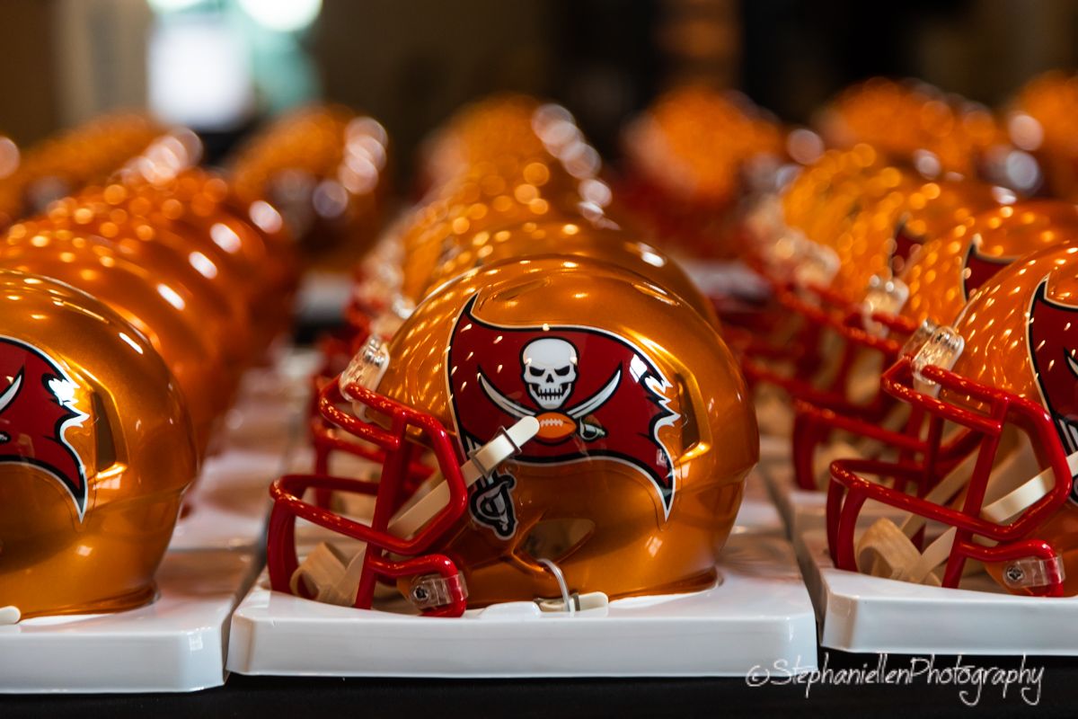 Row of Tampa Bay Buccaneers mini orange football helmets displayed on white stands.
