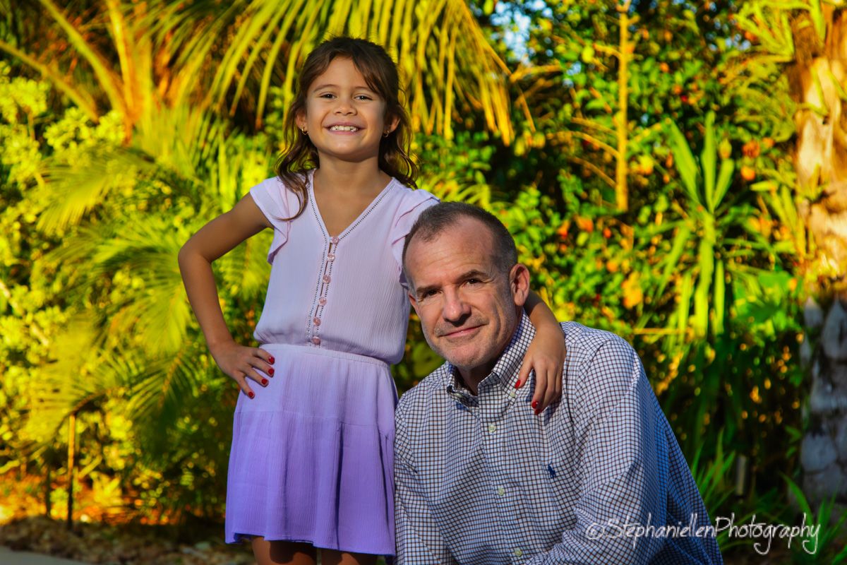 A smiling man and young girl pose together in a lush tropical garden during a professional family photo session.