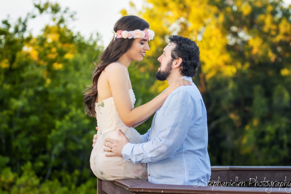 Romantic couple shares a close moment on a wooden railing surrounded by lush greenery at golden hour.