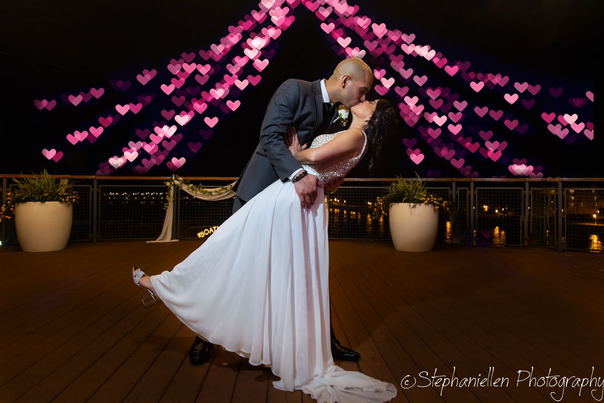 Couple sharing a romantic dip kiss under pink heart-shaped bokeh lights at night.