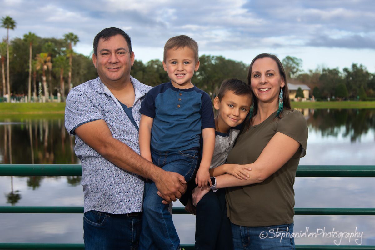 Family of four posing on a bridge with a scenic lake backdrop during an outdoor photography session in Florida.