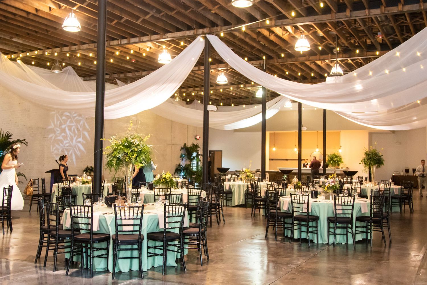 Elegant wedding reception hall with white draping, string lights, and round dining tables.