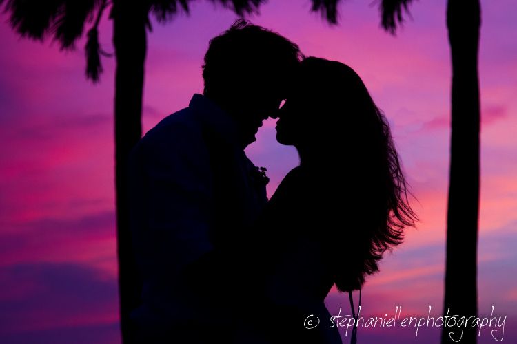 Silhouette of a couple nearly kissing against a vibrant purple and pink sunset sky.