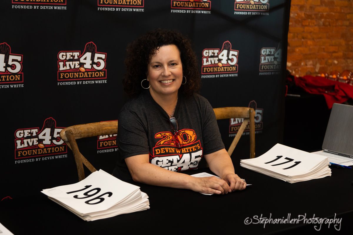 Smiling woman sitting at registration table for Get Live 45 Foundation event.