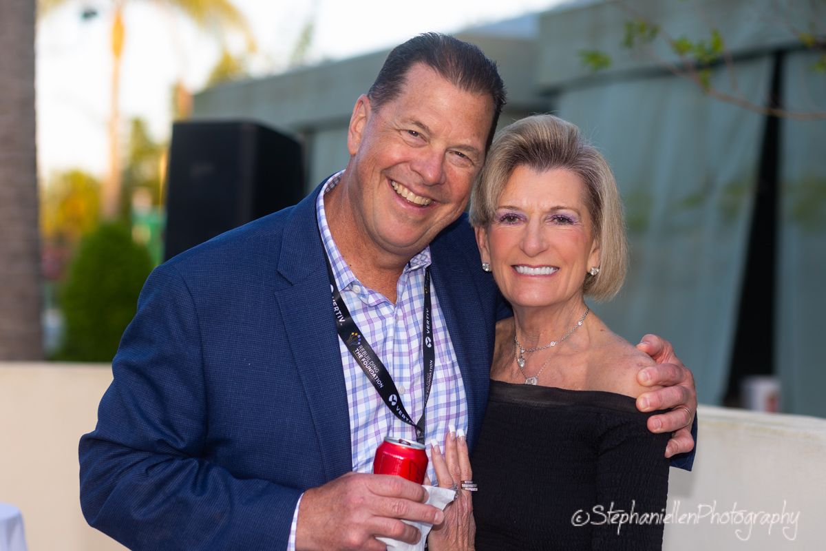 Smiling couple posing together at an outdoor evening event, man holding red can.