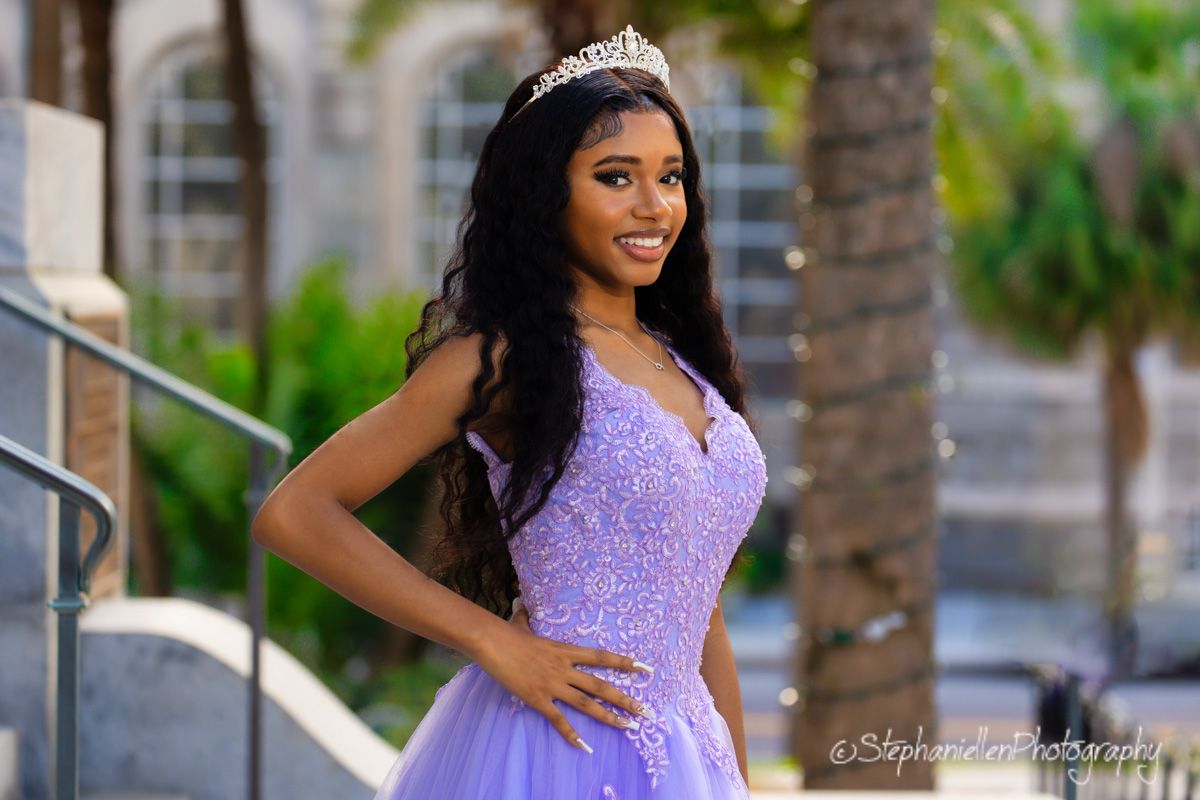 Young woman in lavender quinceañera gown wearing tiara on outdoor staircase.