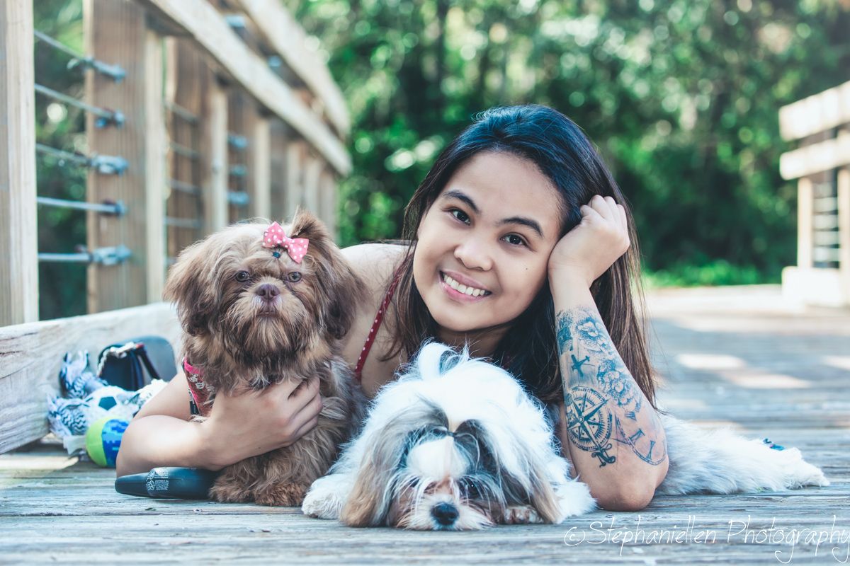 Smiling woman with tattoos poses with two small dogs on a deck.