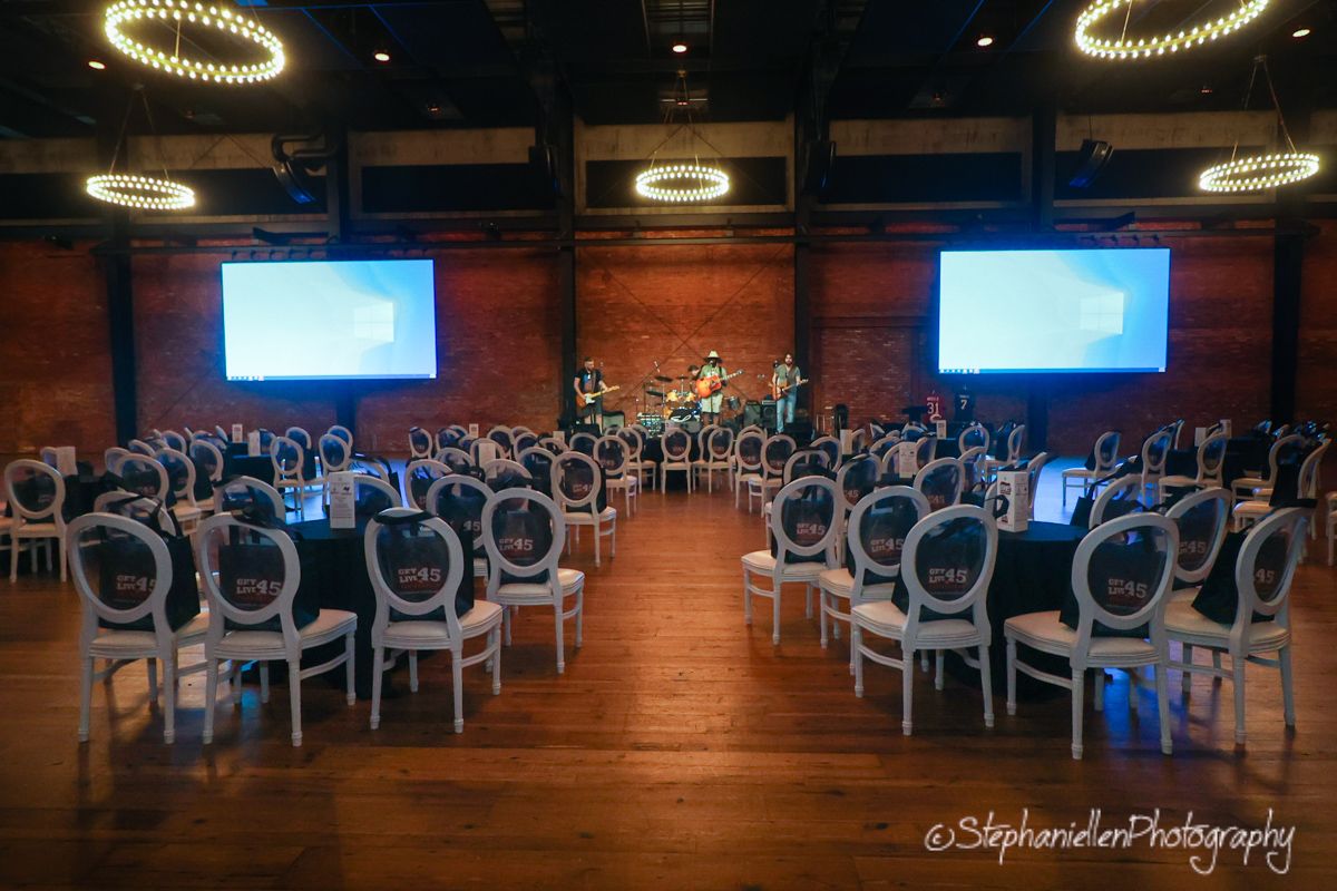 Elegant event venue with white chairs, brick walls, and dual projection screens.