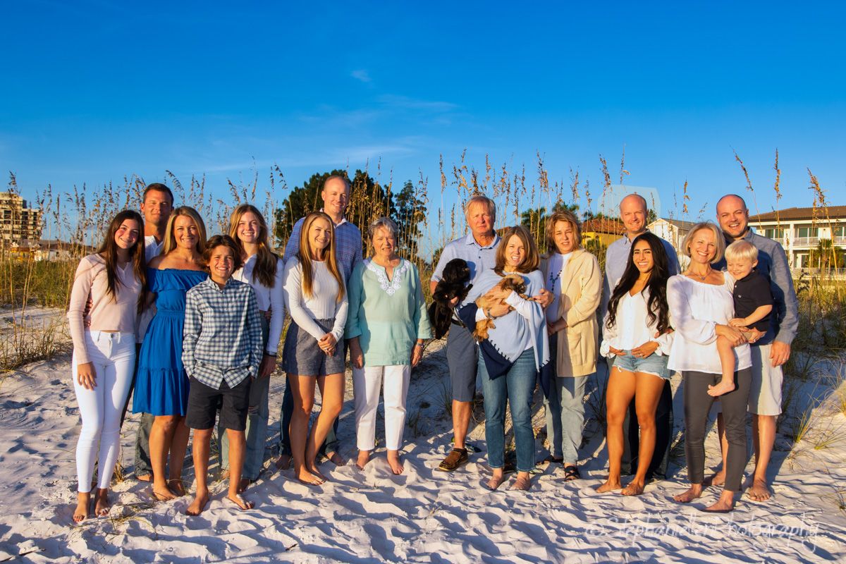 Large family group portrait on a sunny beach with white sand and sea oats in the background.
