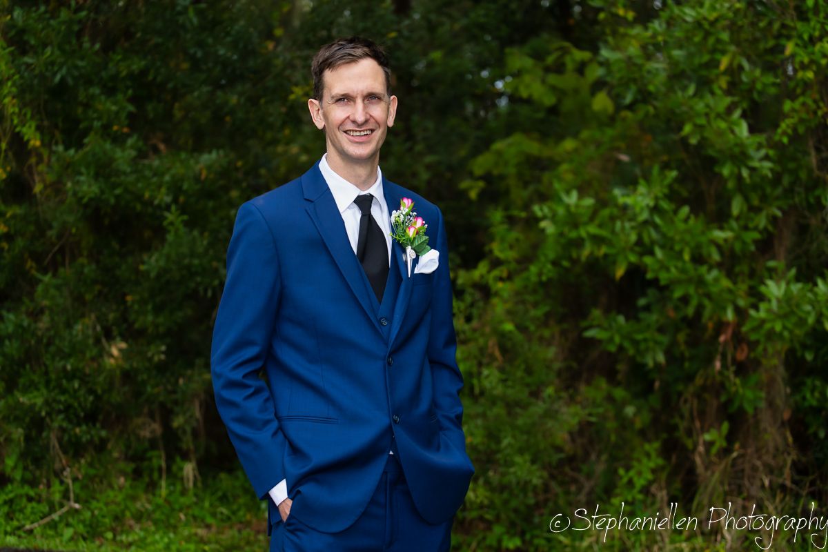 Handsome groom in a royal blue suit with a floral boutonniere smiling outdoors at his wedding.