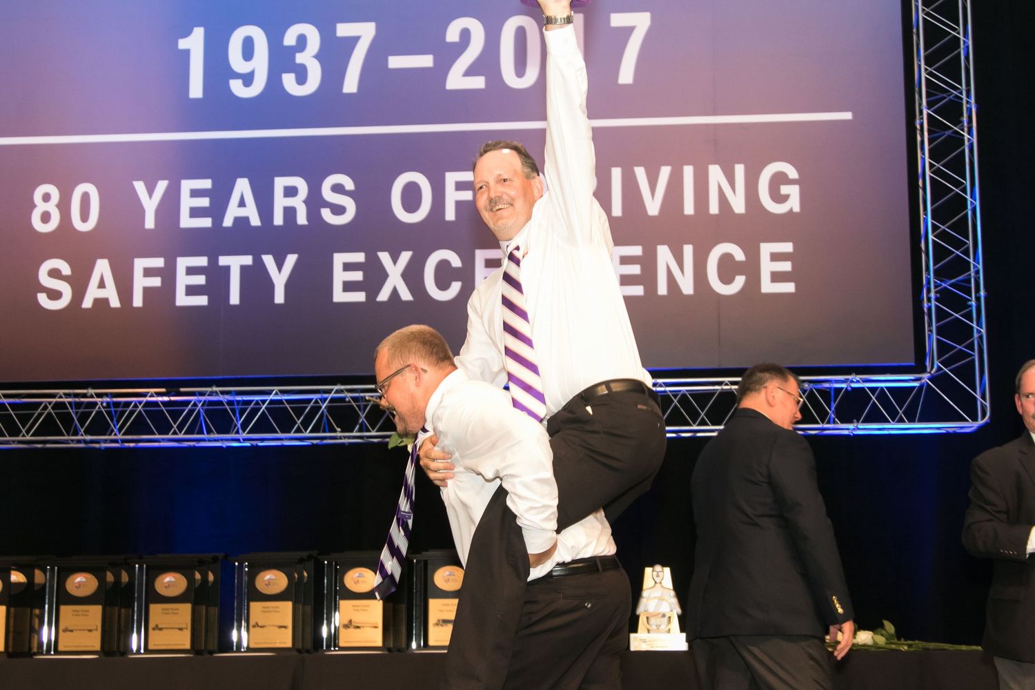 Man raises arm in celebration on stage at 80 Years of Driving Safety Excellence anniversary event.