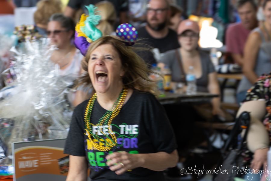Woman in Mardi Gras beads and black tee laughs joyfully at a festive outdoor celebration.