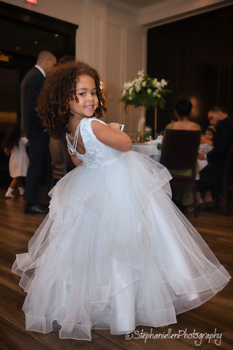 Adorable flower girl in a white tulle ball gown twirling at a wedding reception.