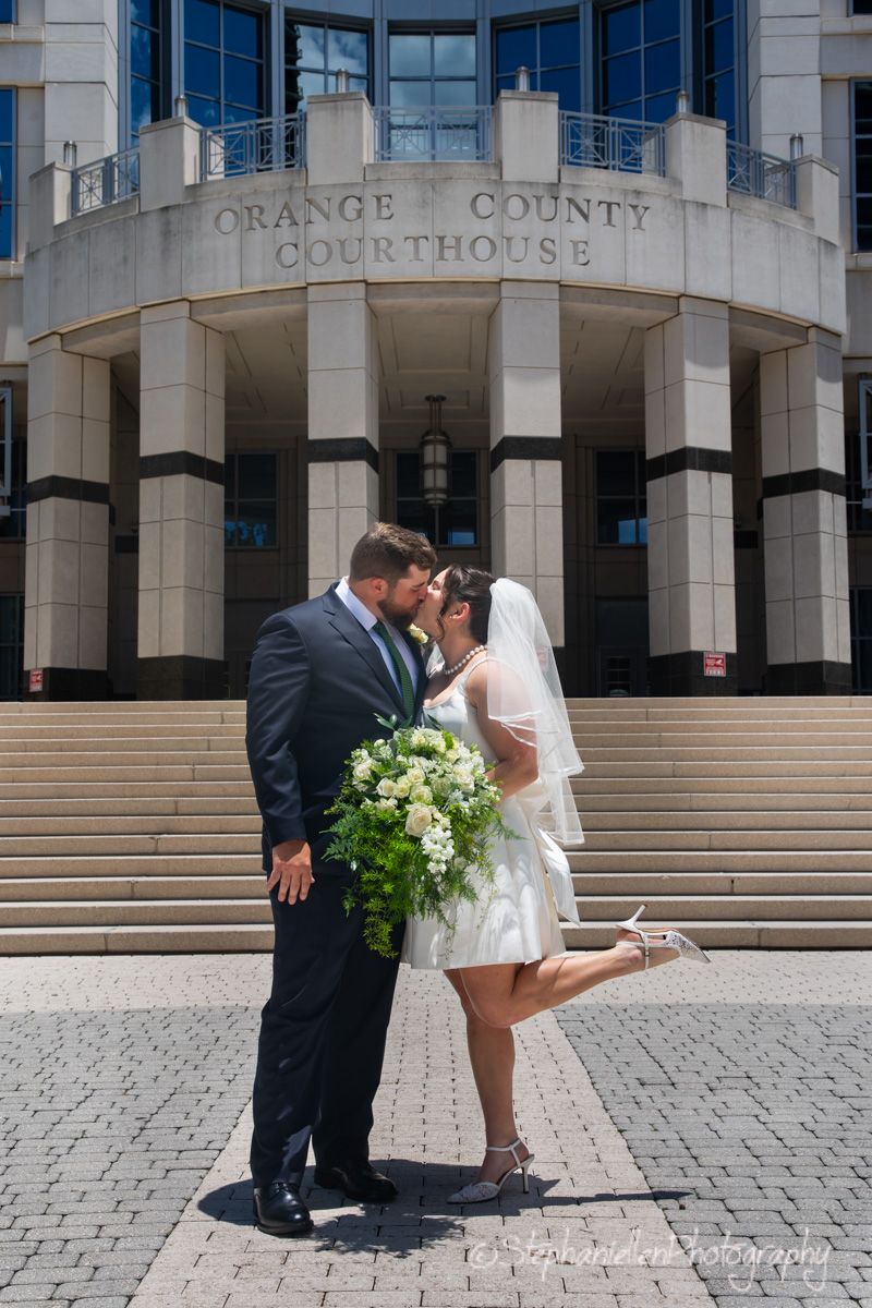 Bride and groom sharing a kiss in front of the Orange County Courthouse on their wedding day.