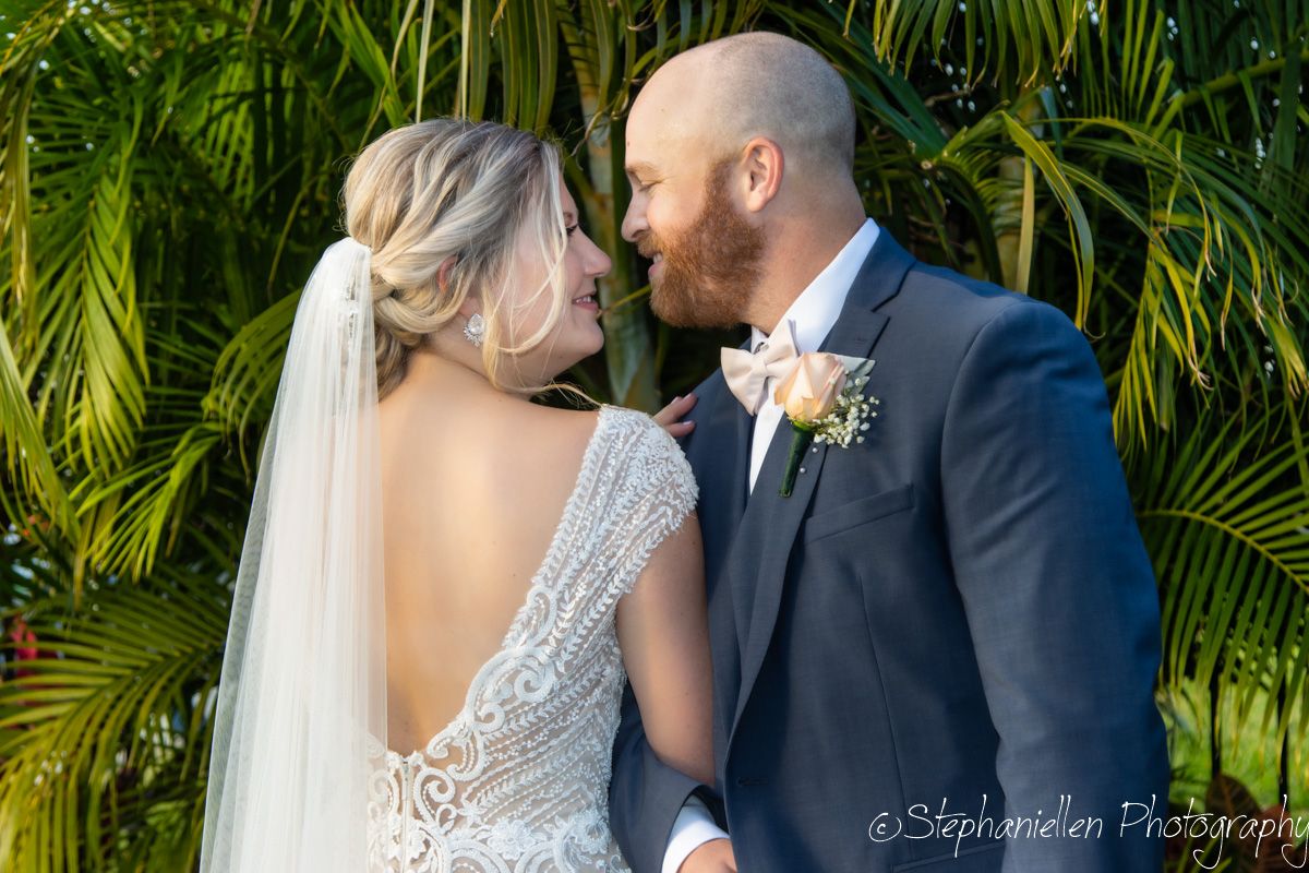 Bride and groom share romantic moment under tropical palm trees, viewed from behind.