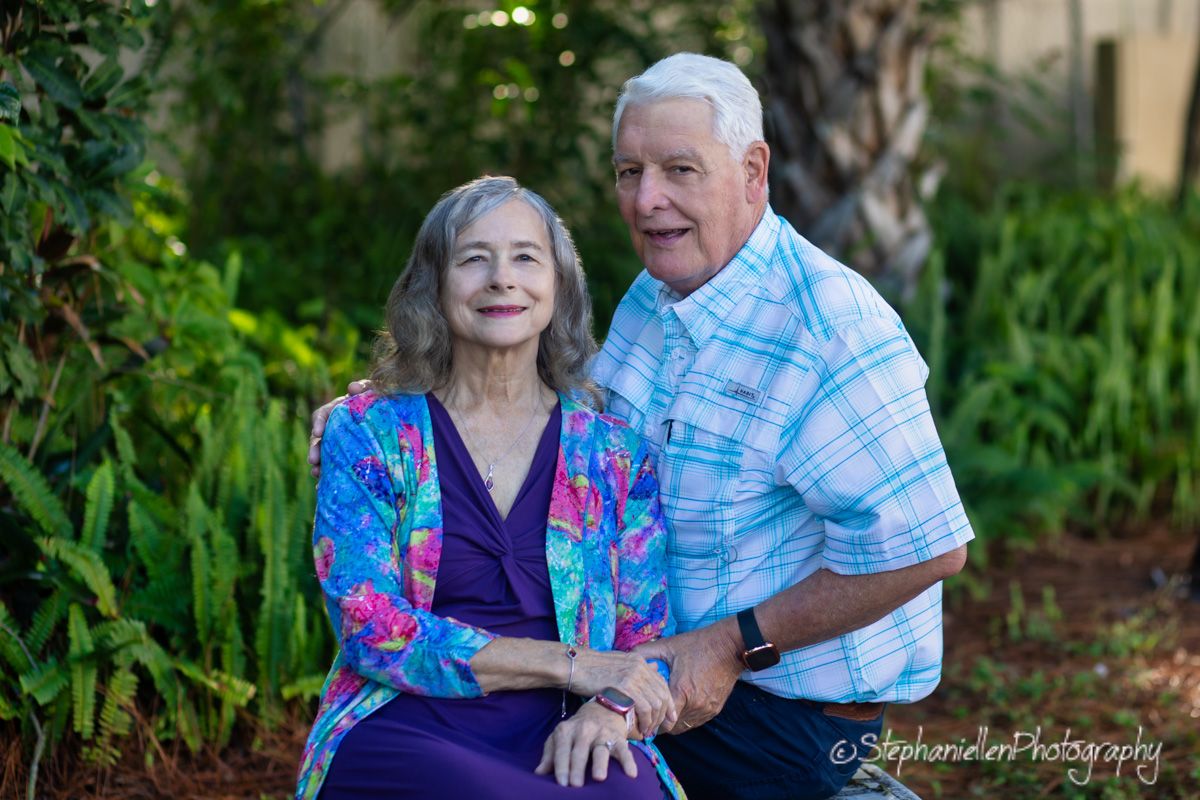 Elderly couple smiling and posing together outdoors in a lush garden setting, professional photography.