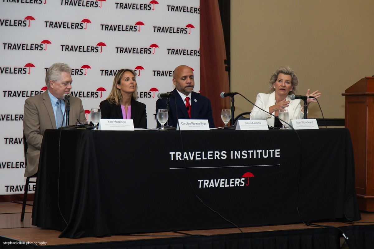 Four panelists seated at a Travelers Institute branded table during a formal discussion.