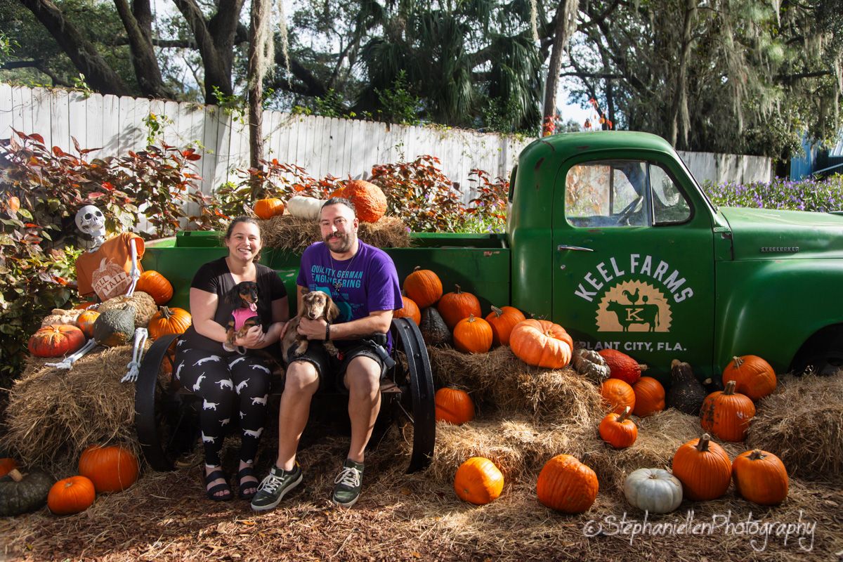Couple sitting on hay bales with pumpkins beside a green Keel Farms truck in Plant City, FL.