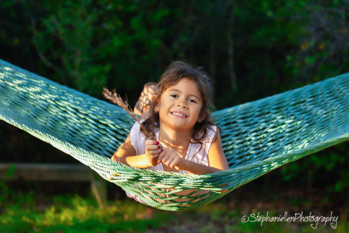 Happy young girl smiling in a green hammock outdoors surrounded by lush green trees.