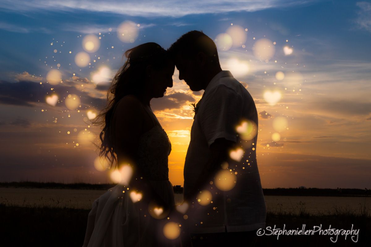 Silhouetted couple touching foreheads at sunset surrounded by dreamy bokeh heart light effects.