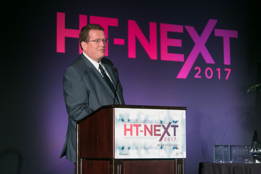 Business speaker presents at HT-Next 2017 conference podium in formal suit.