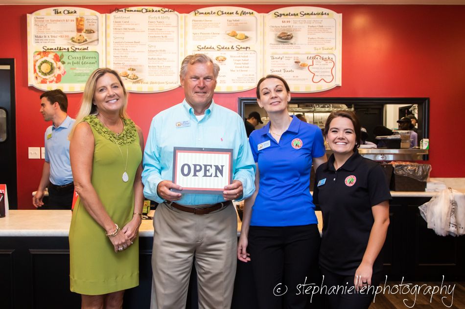 Four people pose with Open sign at new restaurant grand opening ceremony.