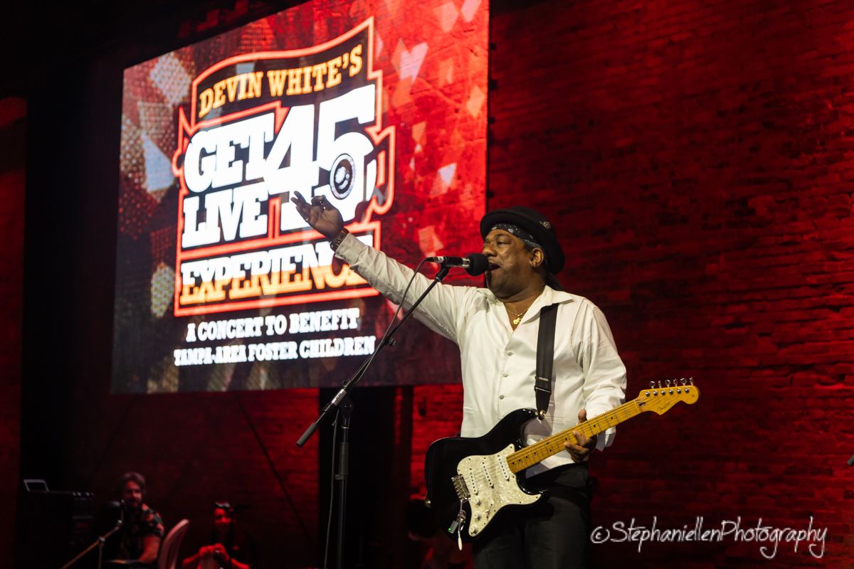 Performer playing guitar on stage at Devin White's Get Live 45 Experience concert.