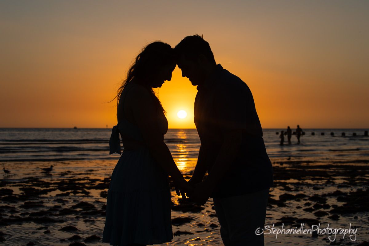 Romantic couple silhouette holding hands on beach during golden sunset.