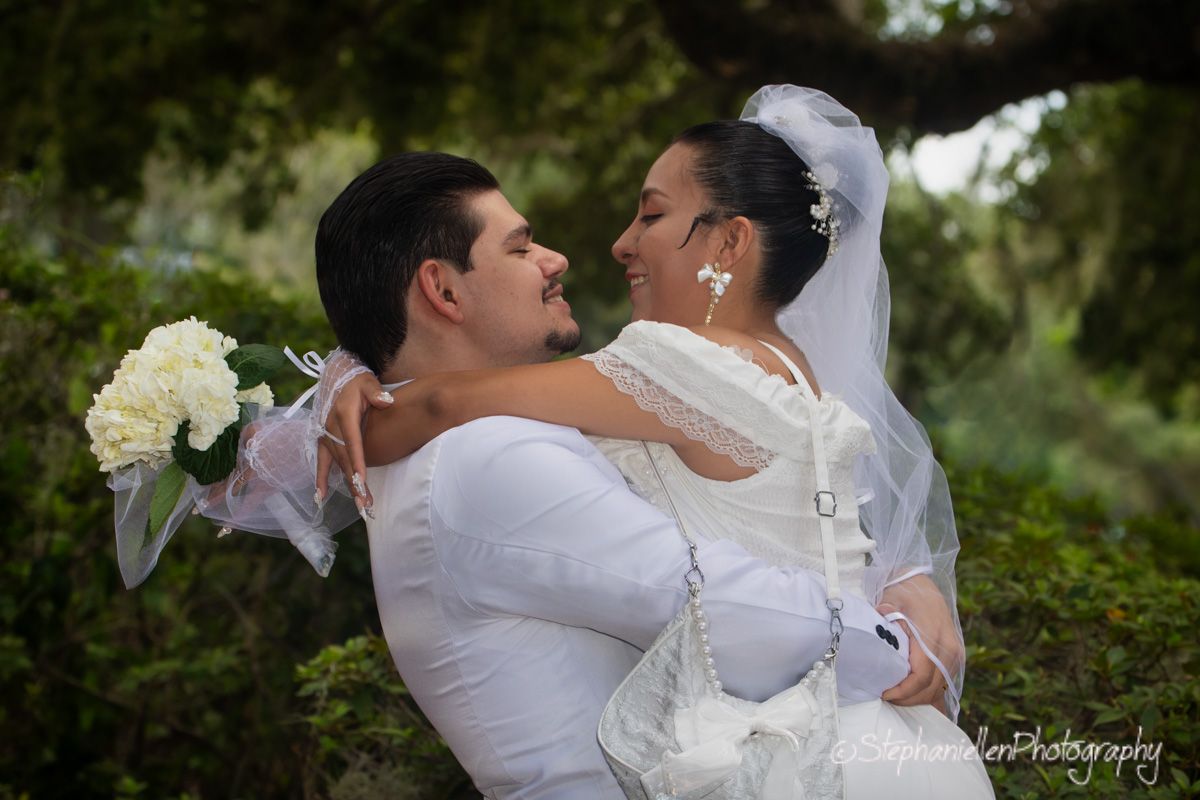 Bride and groom sharing a romantic moment outdoors, bride holding white bouquet in wedding dress and veil.