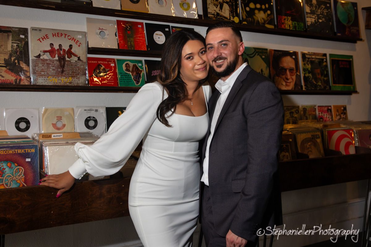 Couple posing together in front of vintage vinyl record wall display at music store.