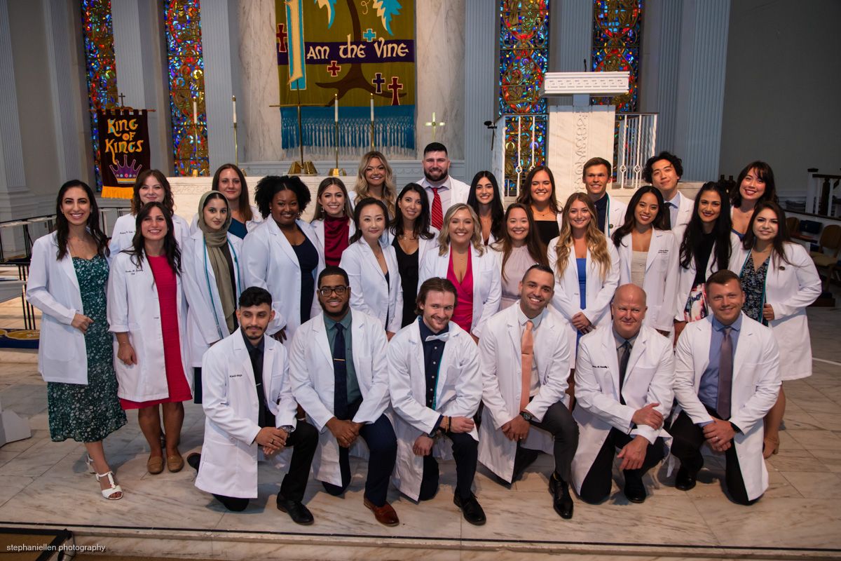 Large group of medical professionals in white coats pose together inside a decorated church.