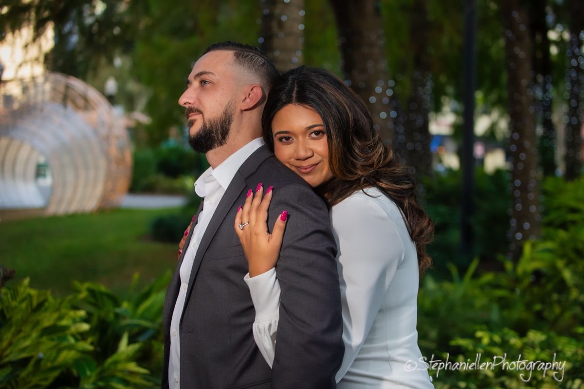 Couple posing back-to-back outdoors at sunset surrounded by tropical green foliage.