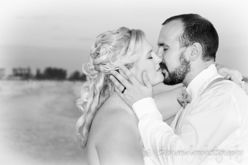 Black and white romantic wedding photo of bride and groom sharing a tender kiss outdoors.