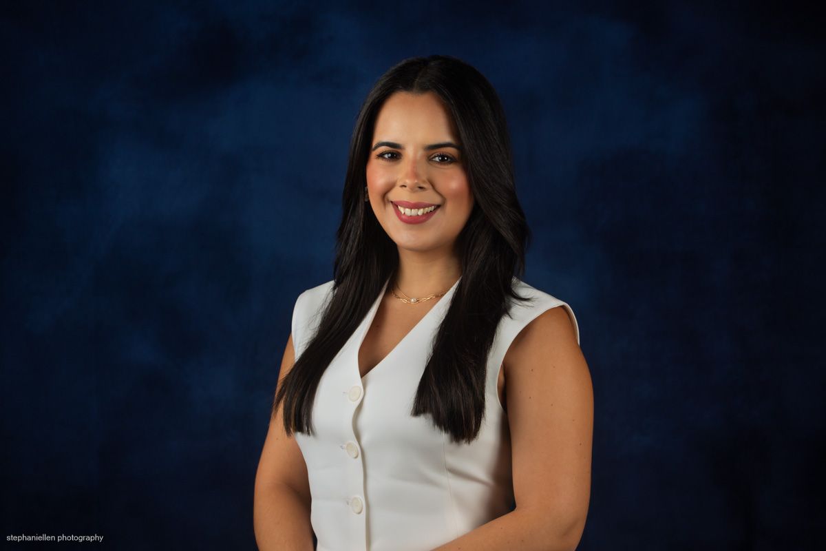 Professional headshot of a young woman in white sleeveless top against blue background.