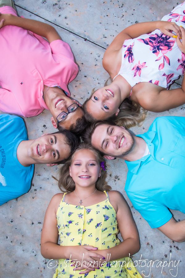 Five smiling people lying in a circle on the ground, heads together, photographed from above by StephanieLen Photography.