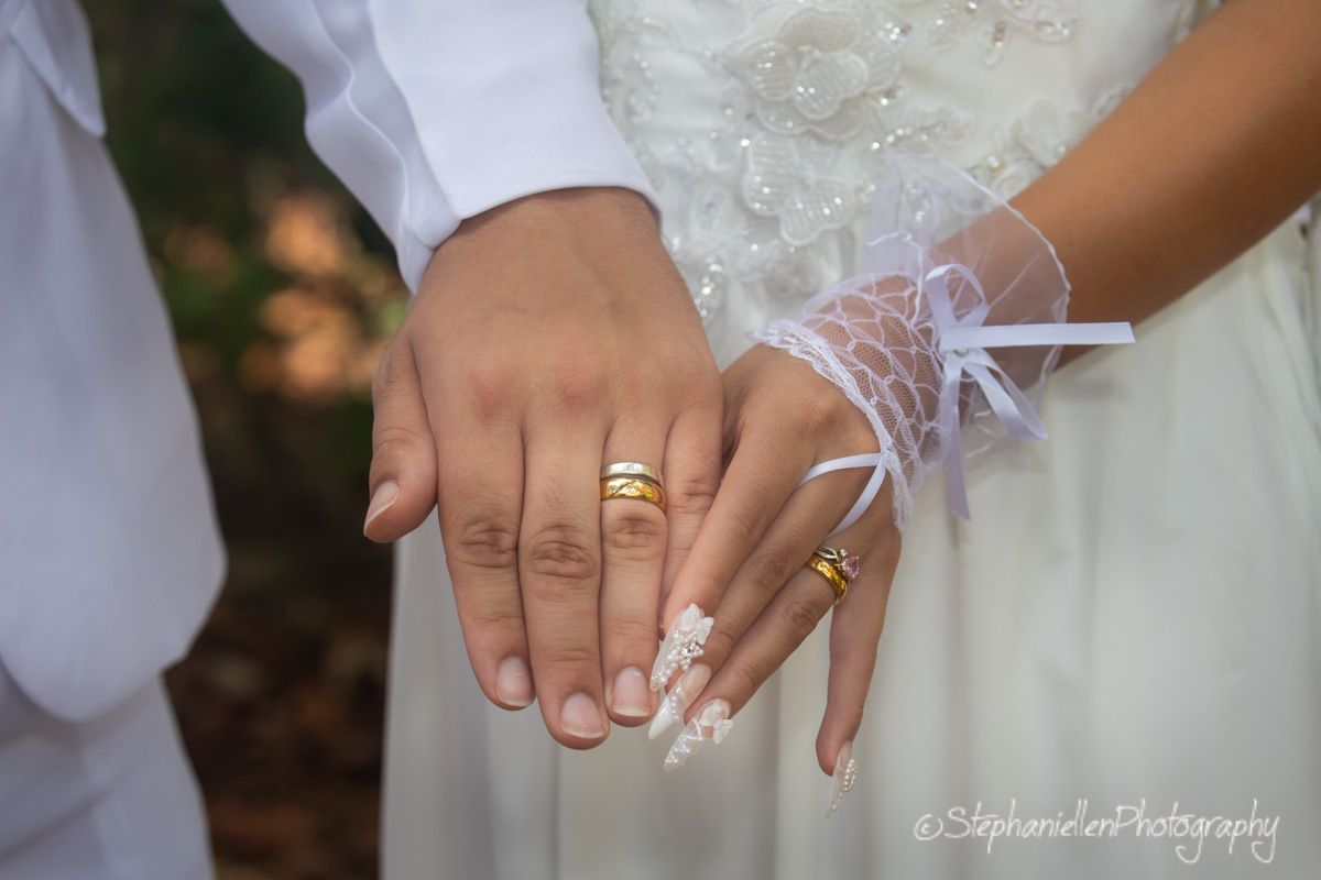 Close-up of bride and groom hands showing gold wedding rings, bride wearing lace glove accessory.