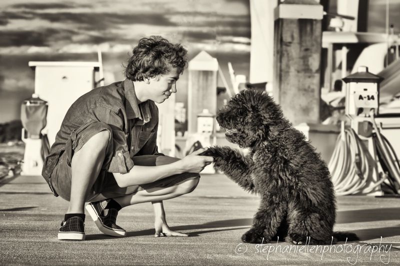Child crouching to interact with a black cat outdoors in black and white photo.