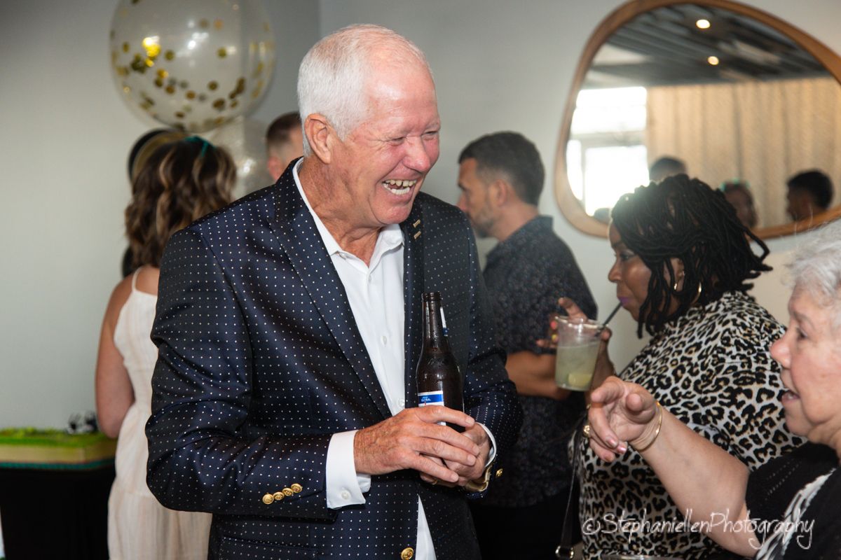 Elderly man laughing and socializing at a casual indoor celebration party.