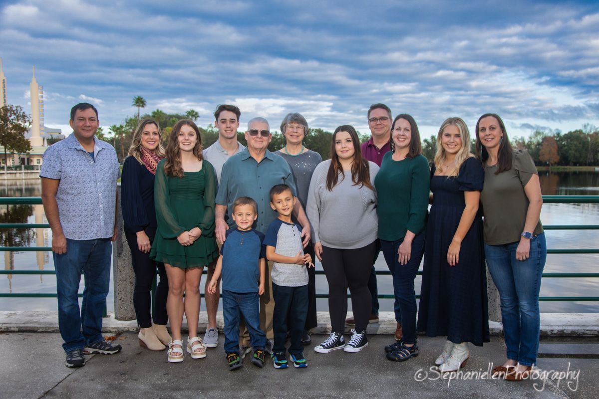 Large family group portrait on a bridge with a scenic lake and landmark in the background.