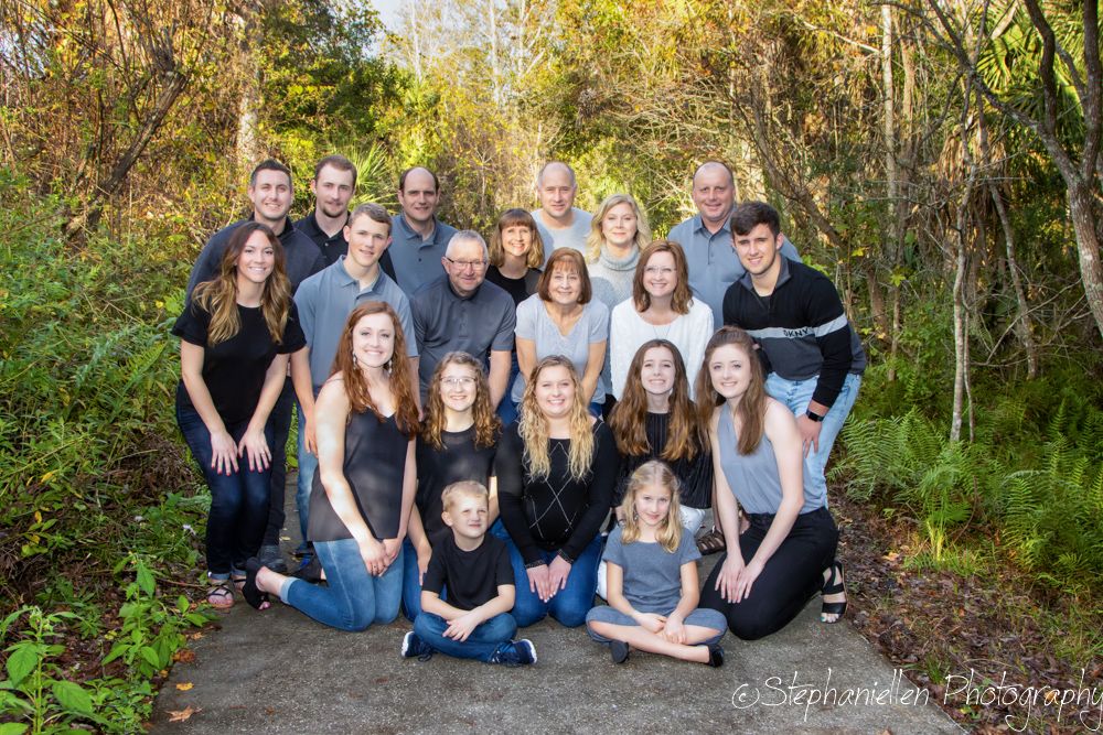Large family group portrait outdoors on a stone path surrounded by lush green trees and foliage.