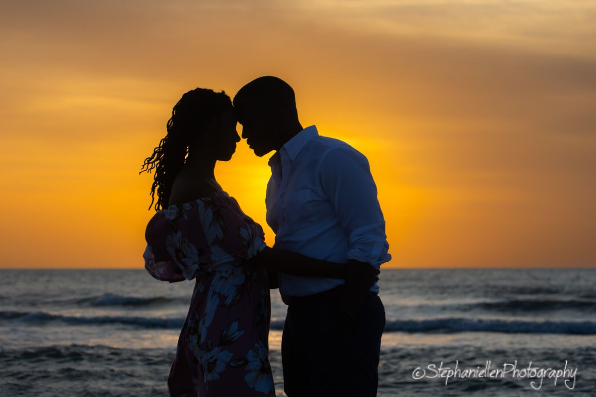 Romantic couple silhouetted against a stunning golden sunset on the beach, sharing an intimate moment.