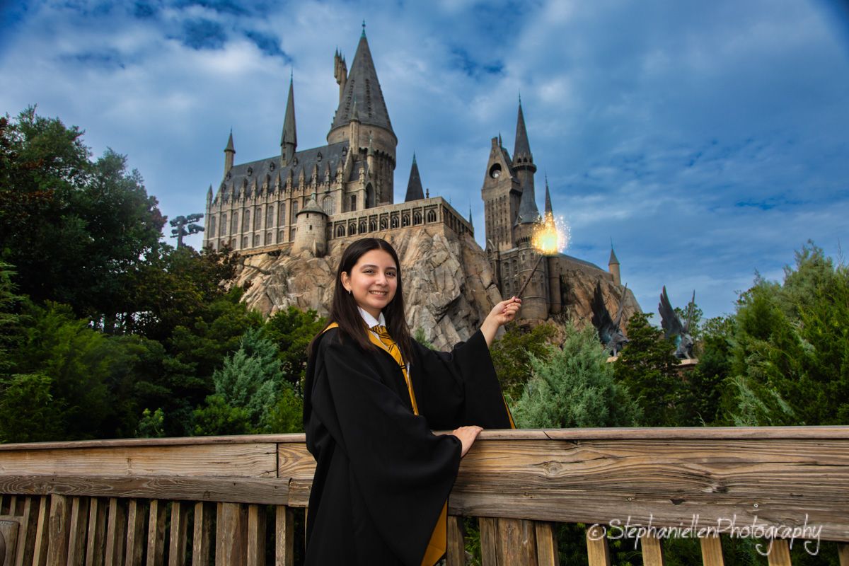 Woman in Hogwarts robe holding a wand poses in front of Hogwarts castle at Universal Studios.