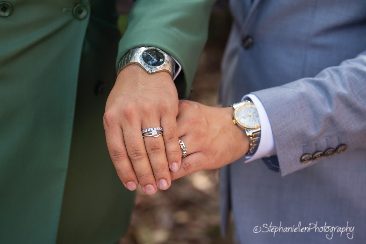 Newlyweds displaying their wedding rings while holding hands, both wearing elegant wristwatches.