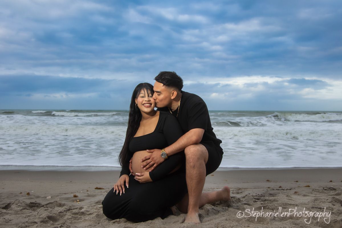 Couple sharing a tender maternity photo on beach, man kissing woman's cheek while holding her baby bump.