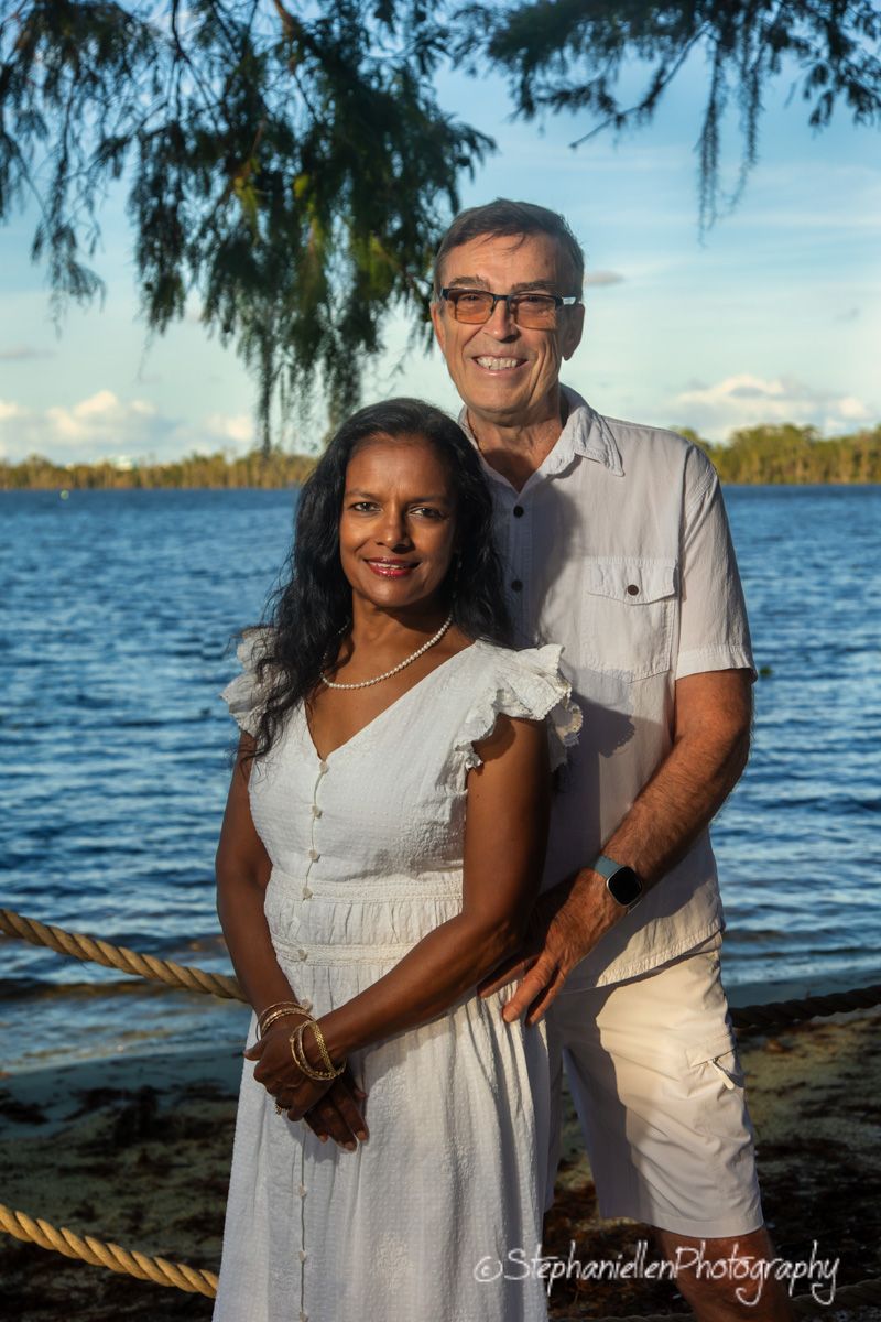 Couple in white outfits posing by a tropical waterfront at sunset, photographed by StephanieEllen Photography.