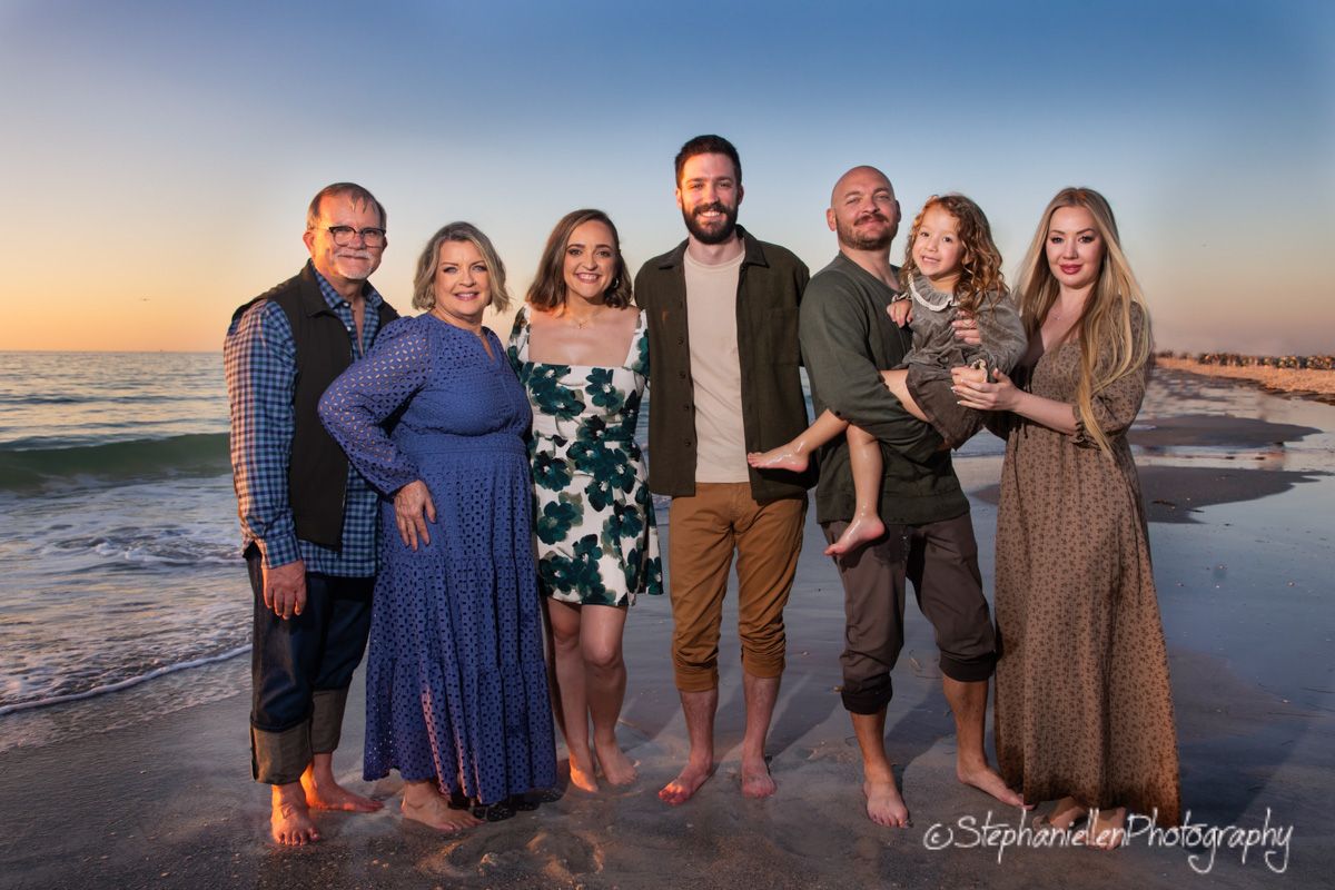 Family of seven posing together on a beach at sunset with ocean waves in the background.