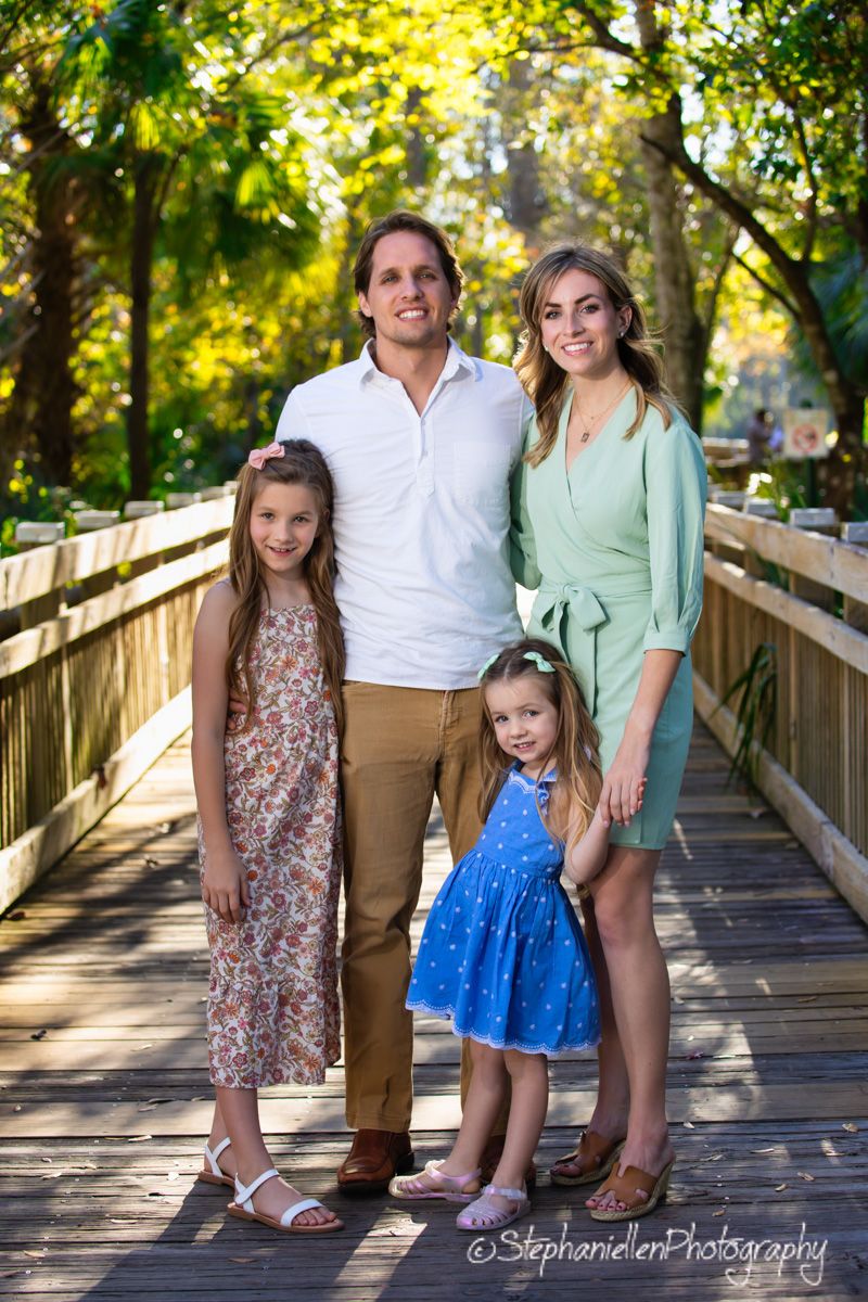 Happy family of four posing on wooden bridge surrounded by lush green trees.