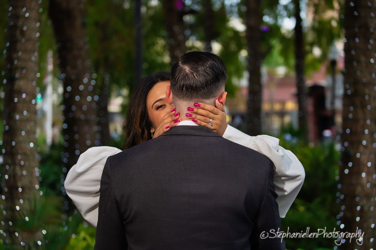 Woman embracing man from behind outdoors among trees with sparkling bokeh lights.